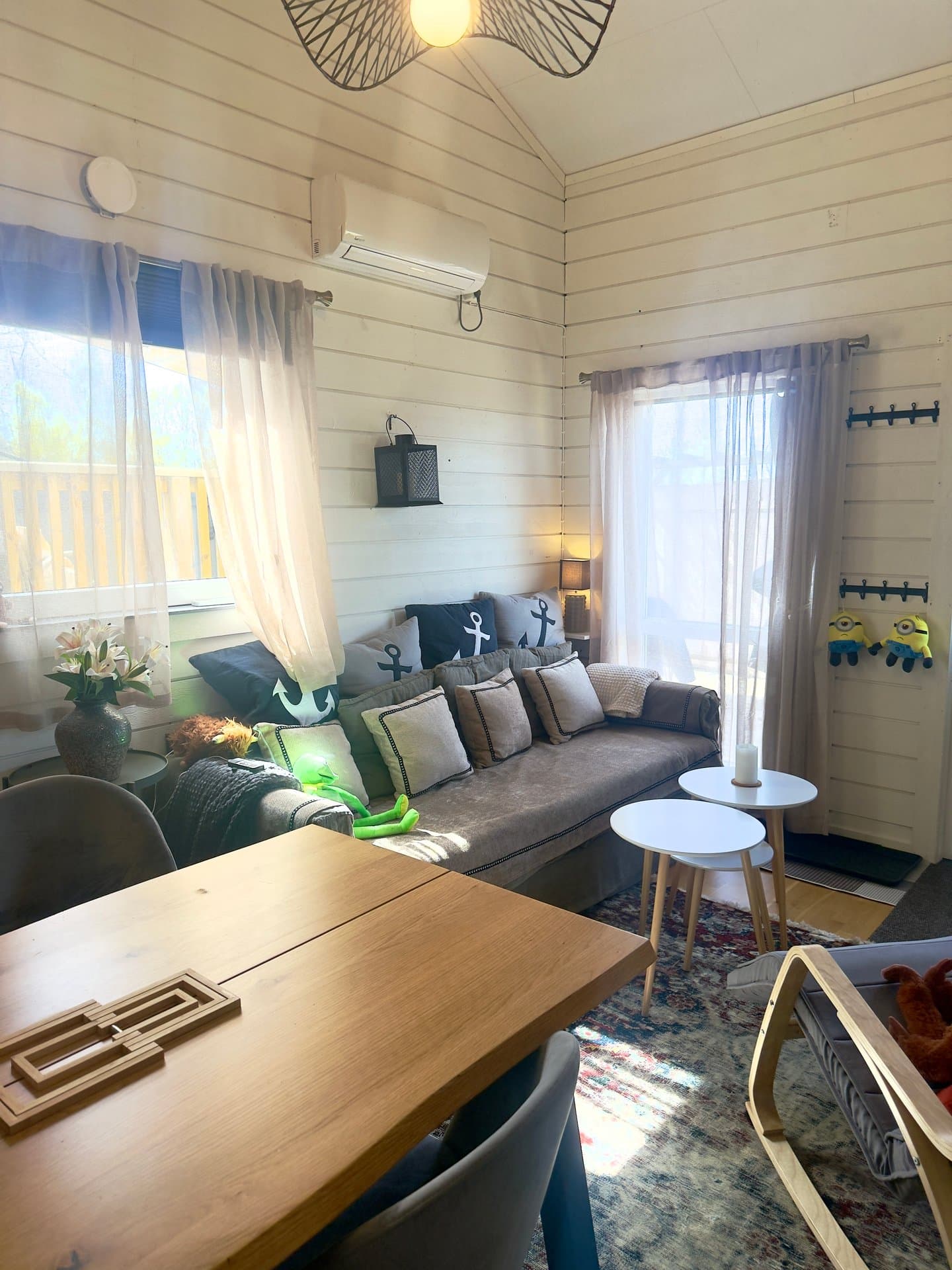 Mysig vardagsrum med moderna bekvämligheter, naturligt ljus från stora fönster, bekväm grå soffa med nautiska detaljer och utsikt över omgivningarna. Perfekt för avkoppling och samvaro.